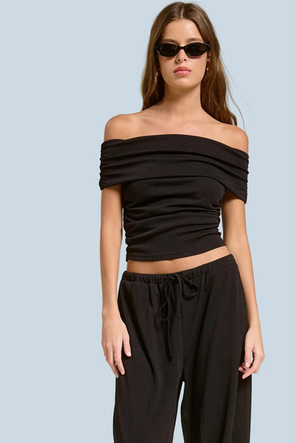 Woman wearing a black off-shoulder top and black pants against a beige background